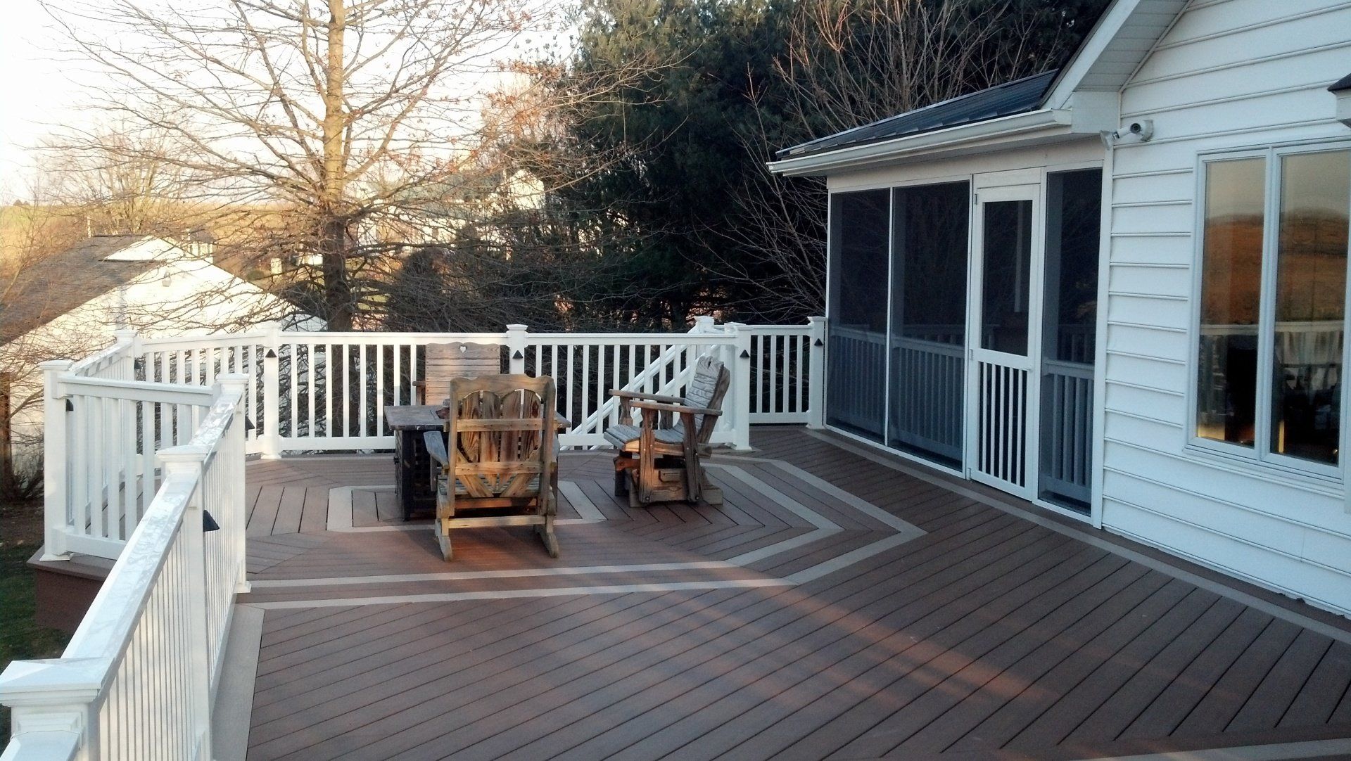 White deck with two rocking chairs, attached to a screened porch, surrounded by trees.