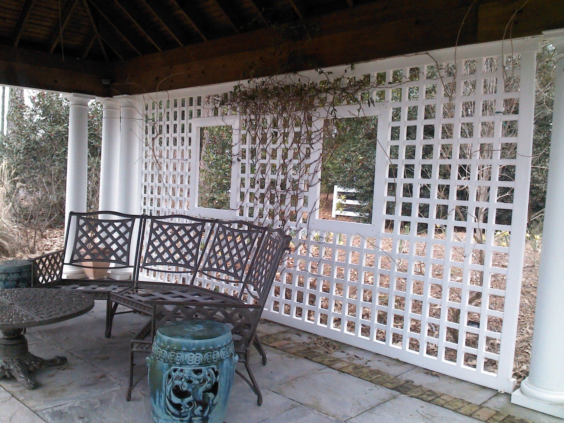 Gazebo patio with white lattice, metal bench, round table, and a blue ceramic stool.