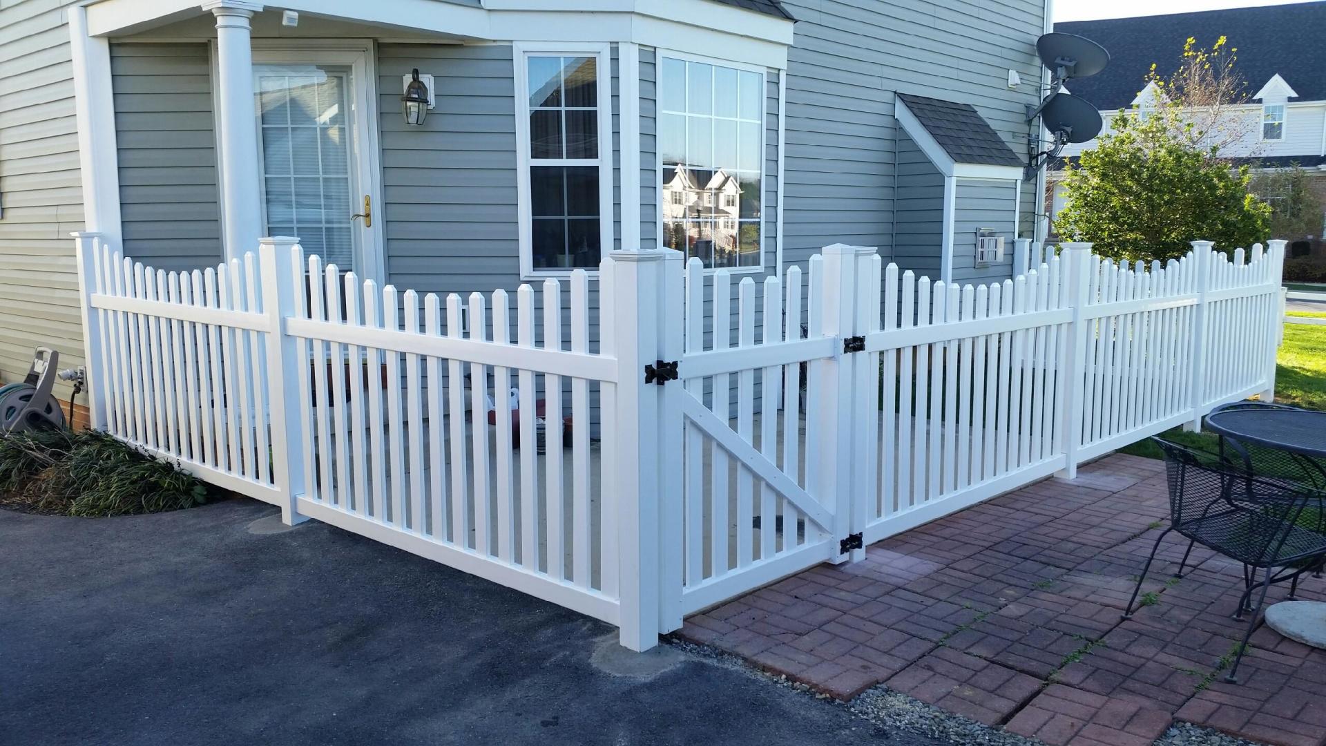 White picket fence surrounding a home's entrance, with a gate, on a brick patio.