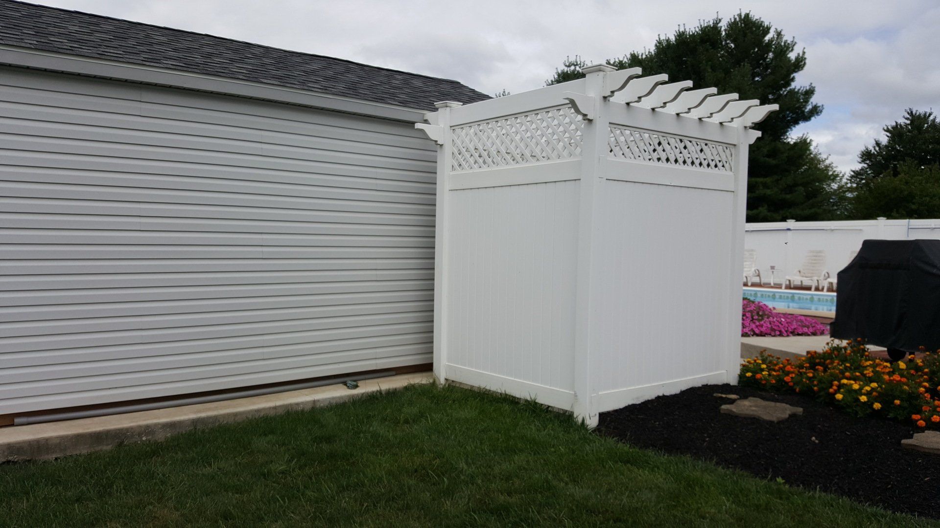 White privacy fence with latticework and pergola top next to a building and grass.