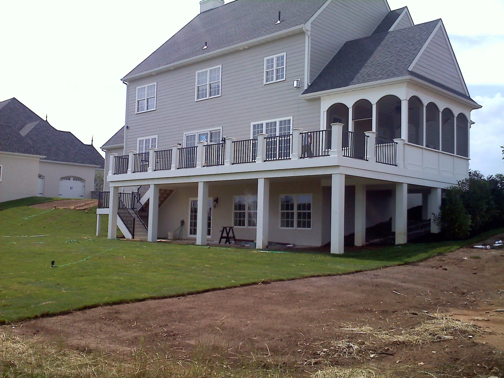 Two-story house with a deck and screened porch. Exterior is tan with a dark gray roof. The house is on a grassy hill.