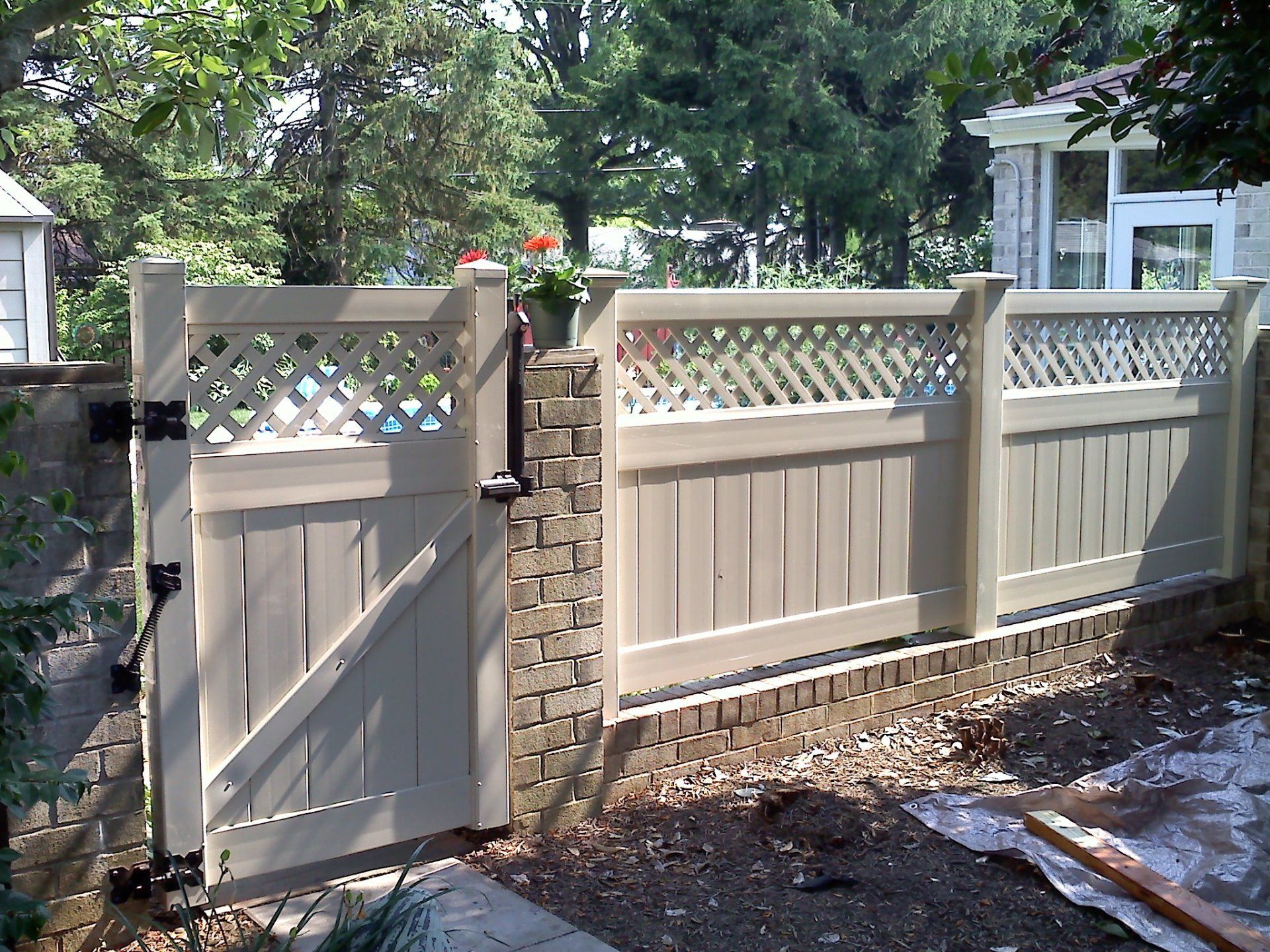 Tan wooden fence with lattice and gate on brick base, flowers on post.