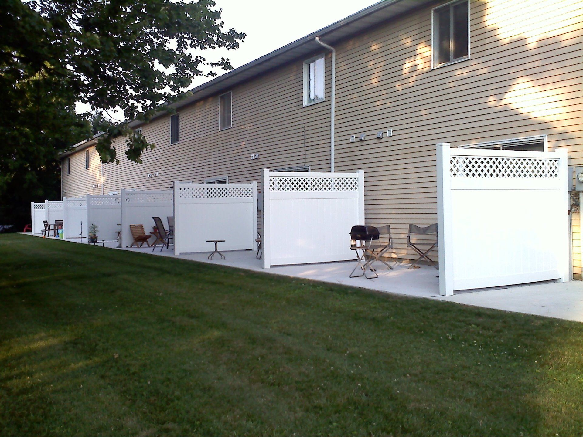 Row of townhouses with white privacy fences, concrete patios, and green lawn.
