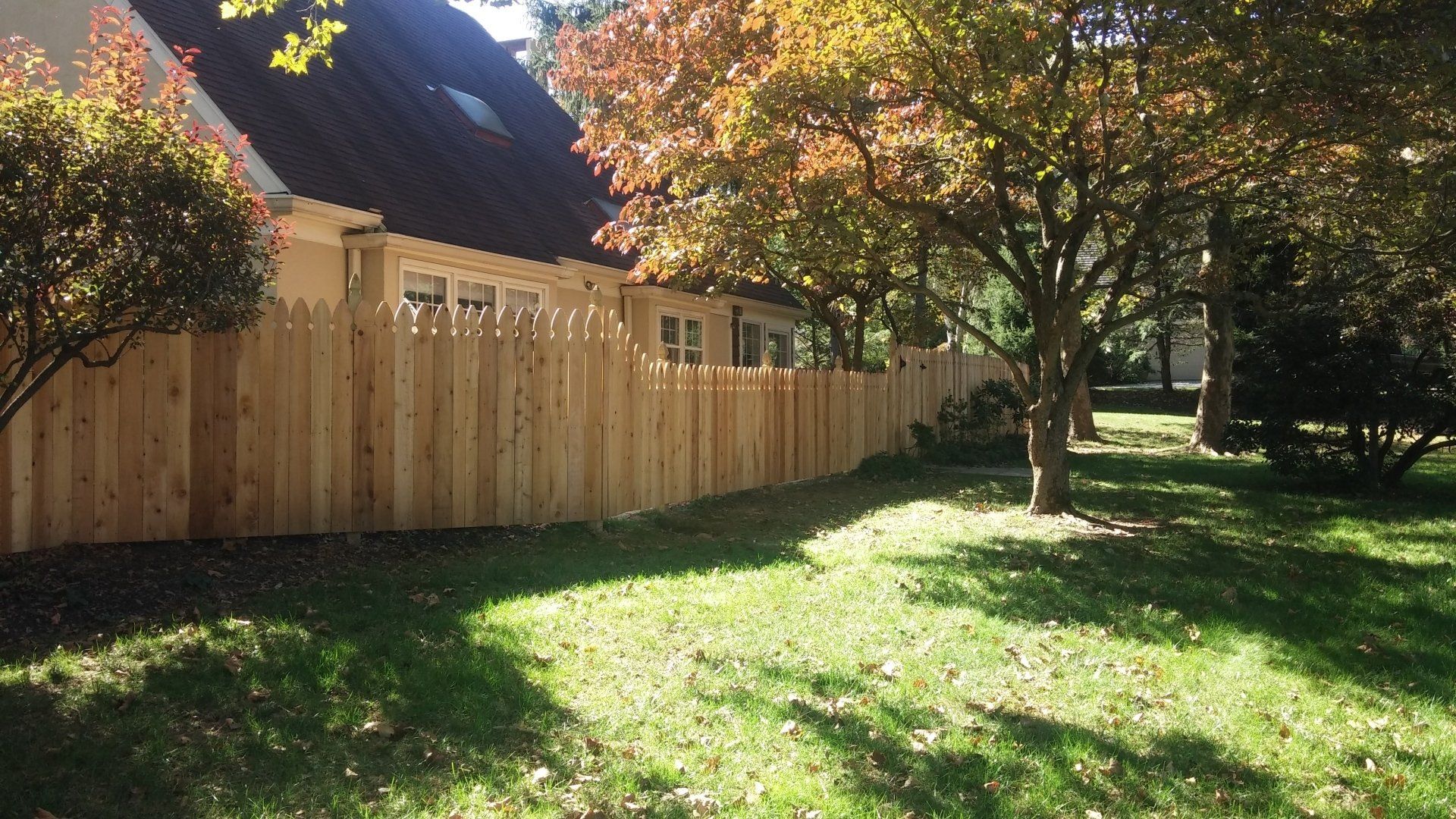 Wooden fence along a house, with fall foliage and green grass.
