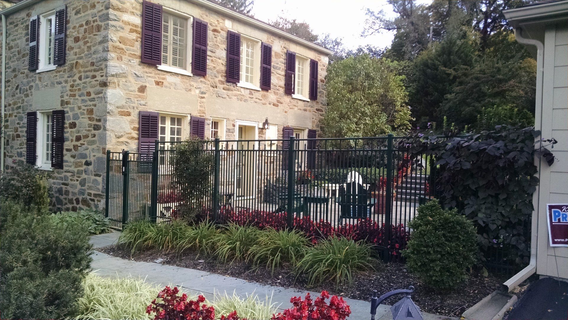 Stone house with dark shutters, enclosed by a black metal fence, surrounded by landscaping in Lancaster, PA.