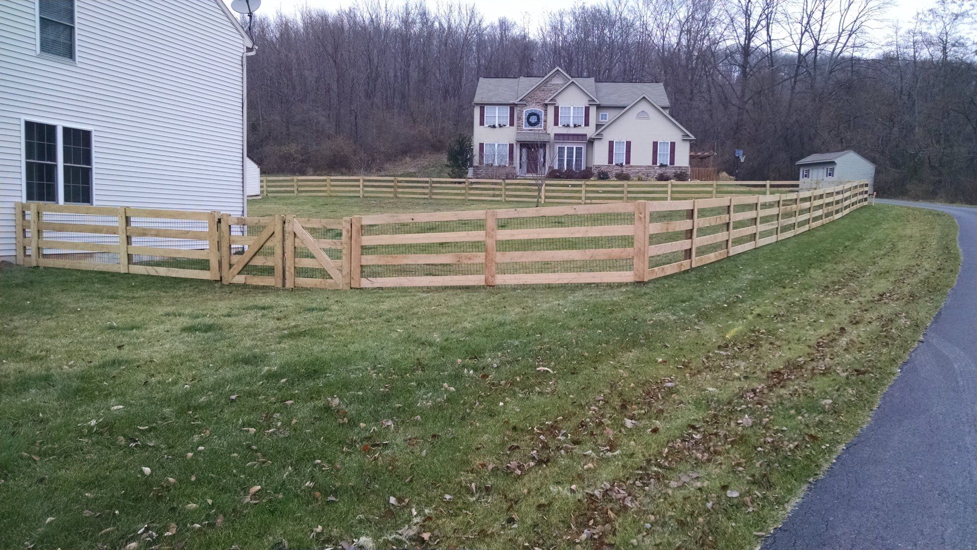 A wooden fence by Millcreek Fence & Decks in Lancaster, PA surrounds a house with a green lawn.