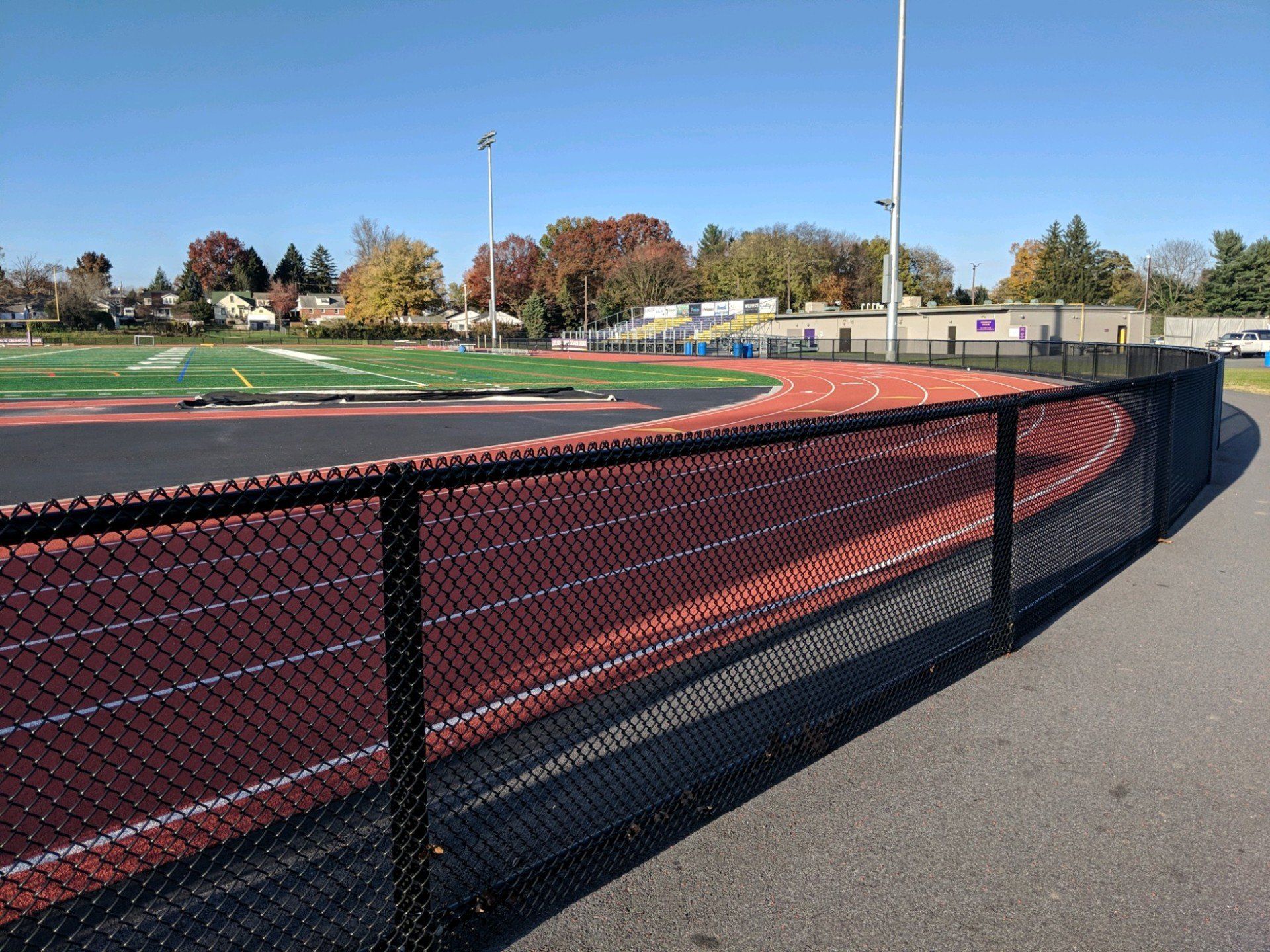 Black chain-link fence bordering a red track and green field under a clear blue sky.