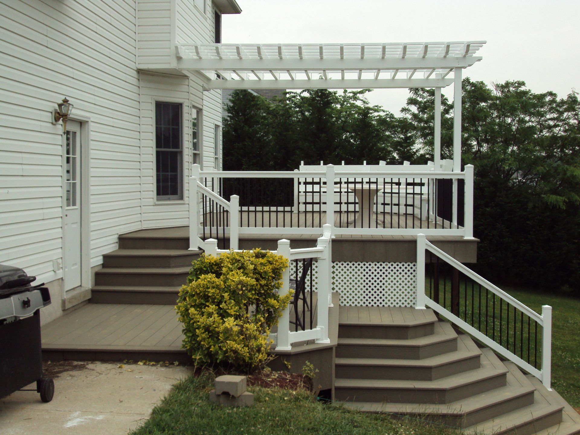White house with composite deck and pergola, steps leading down to yard.