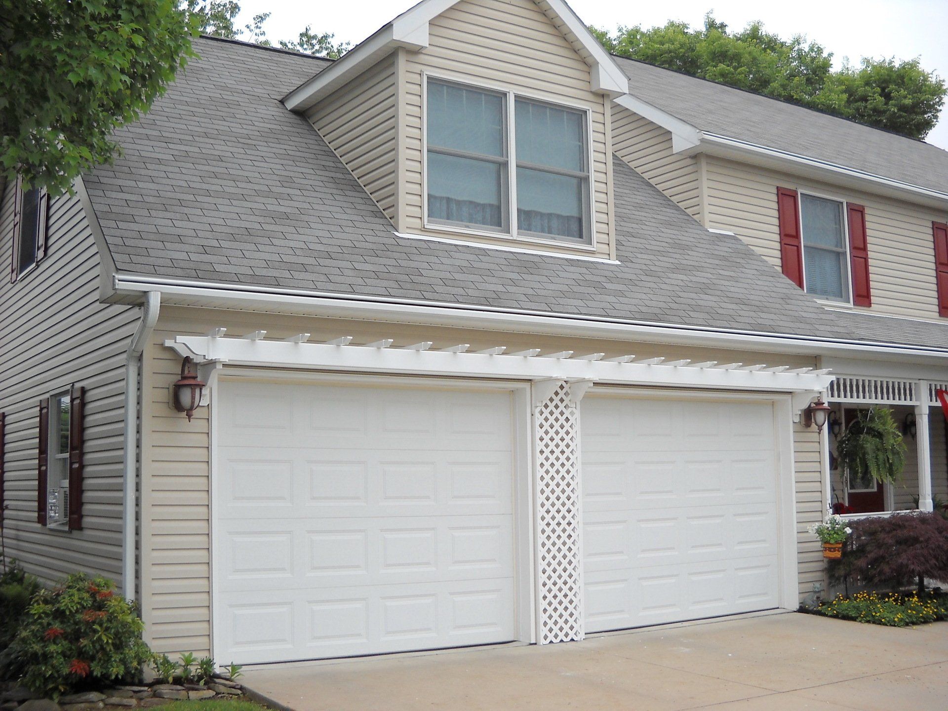 Two-car garage with white doors, tan siding, and a light gray roof on a two-story house.
