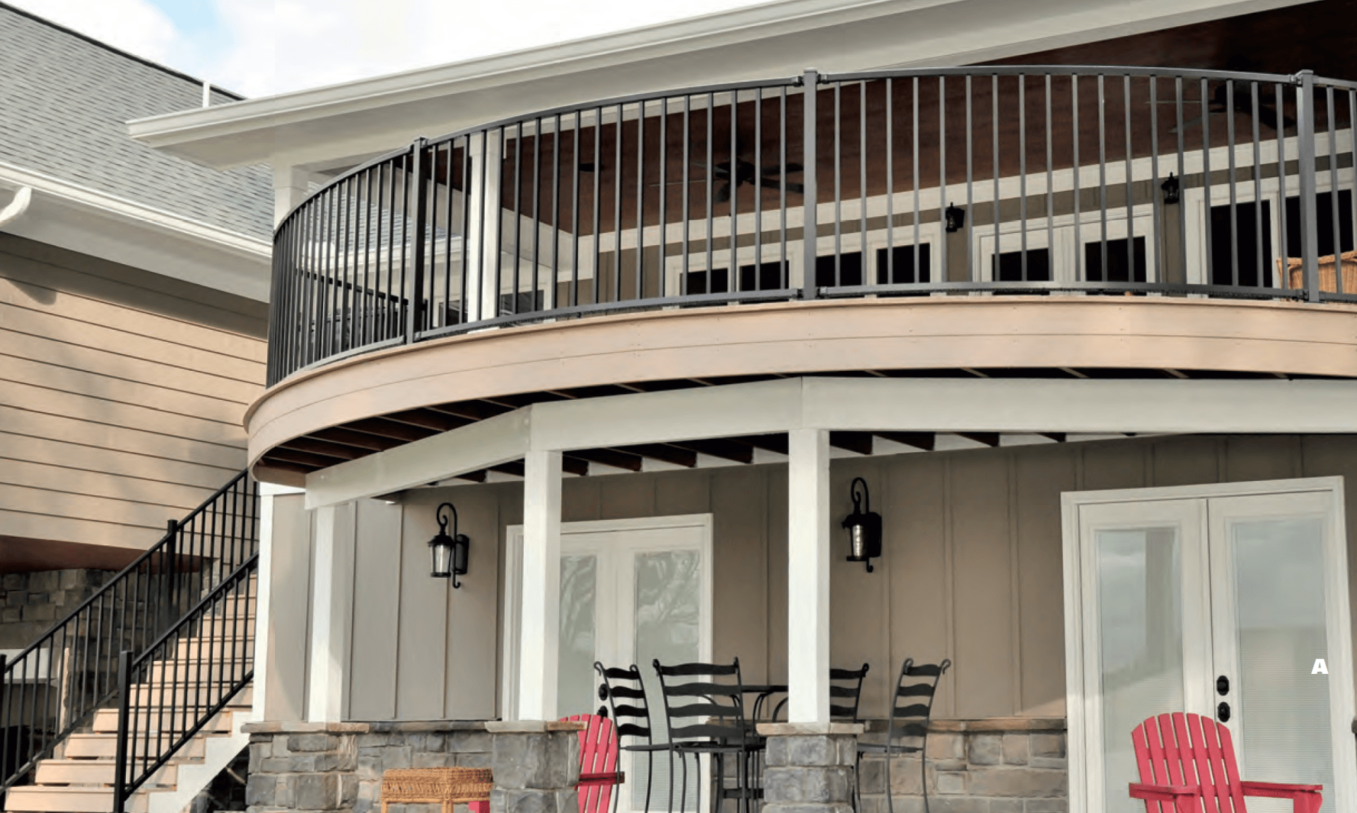 Curved two-story deck with black railings. Bottom level has stone pillars and seating.