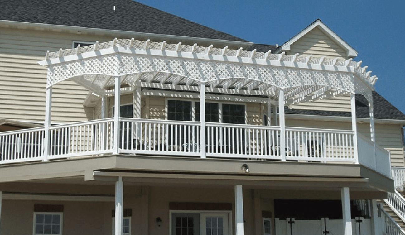 White pergola and railings on a two-story deck, attached to a light-colored house under a blue sky.