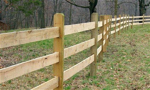 Wooden split-rail fence in a grassy field with trees in the background.