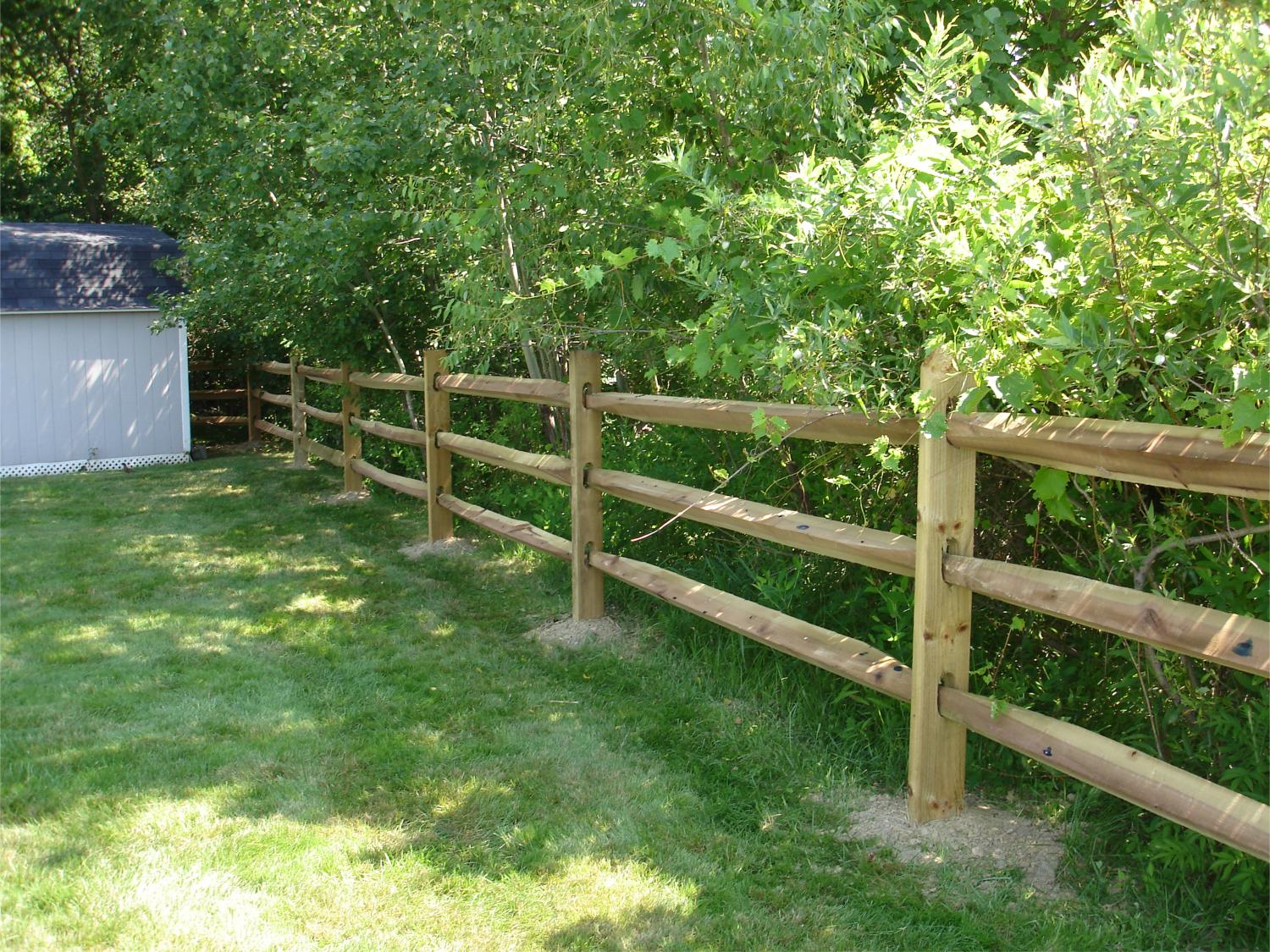 Wooden split-rail fence in a grassy yard, with a small shed and trees in the background.