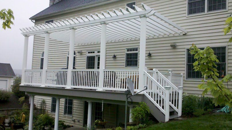 White pergola over a deck attached to a beige house, with stairs and railing.