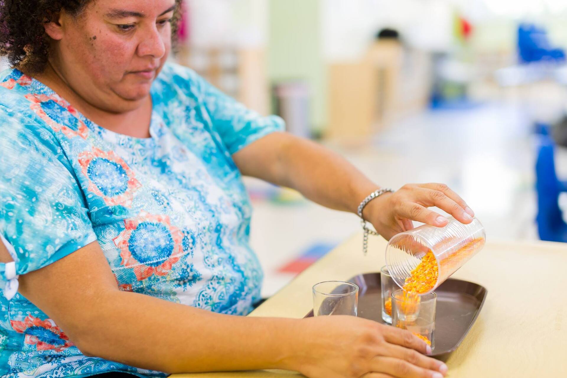 A woman is pouring liquid into a glass while sitting at a table.