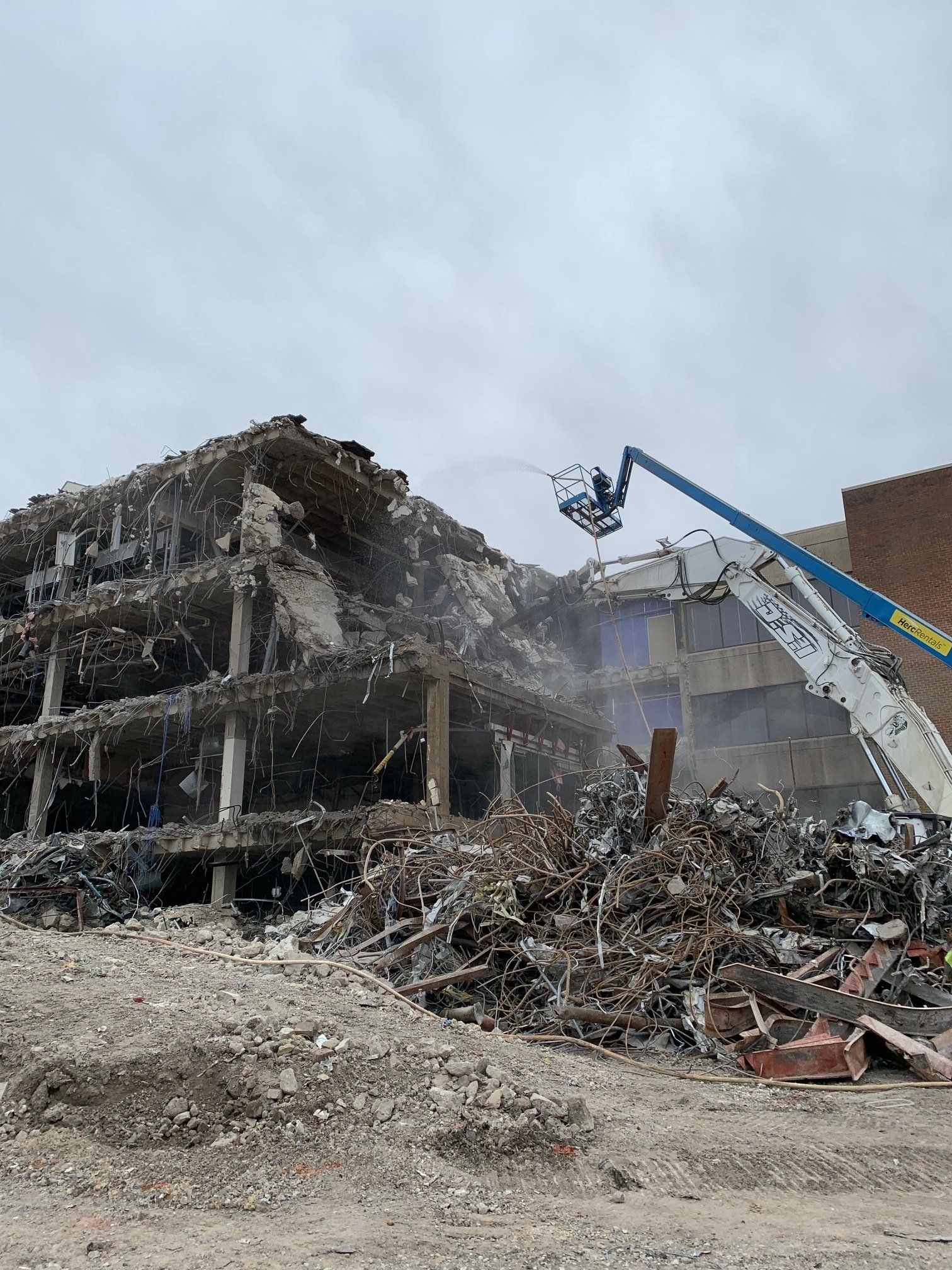 Demolition of a damaged concrete building, with a crane lifting debris amid rubble.