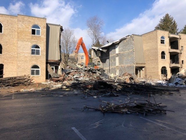 Demolished apartment buildings with rubble in front and an orange excavator in the background