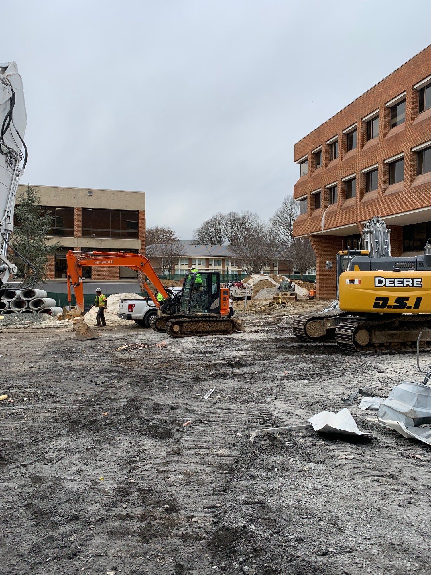 Construction site with excavator and dump truck clearing rubble beside damaged brick buildings