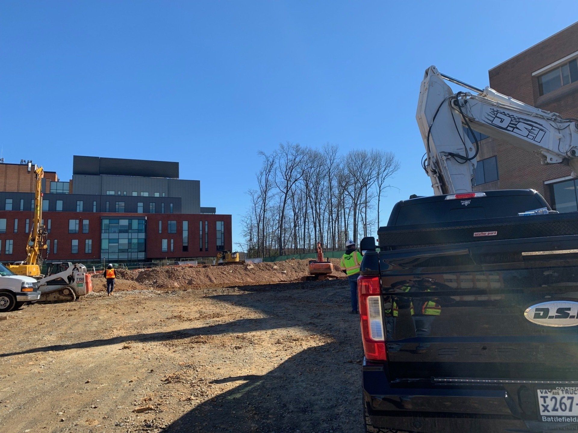 Construction site with excavator and pickup truck beside a modern building under a clear blue sky