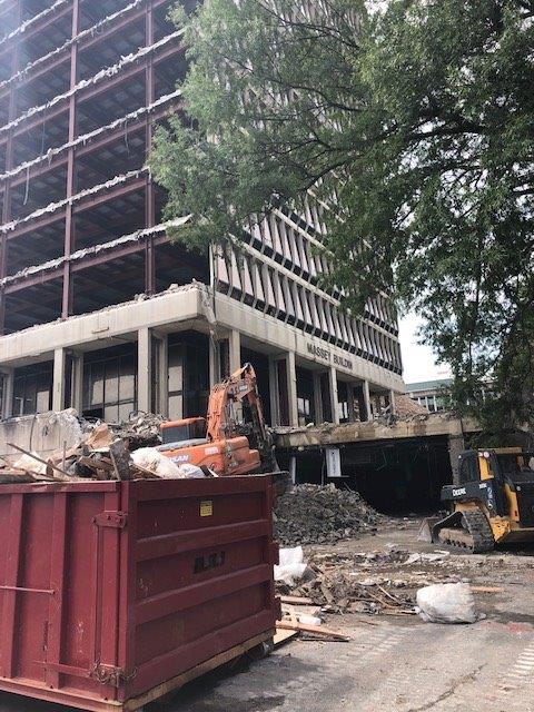 Construction rubble and machinery beside a partially demolished building with a red dumpster in front