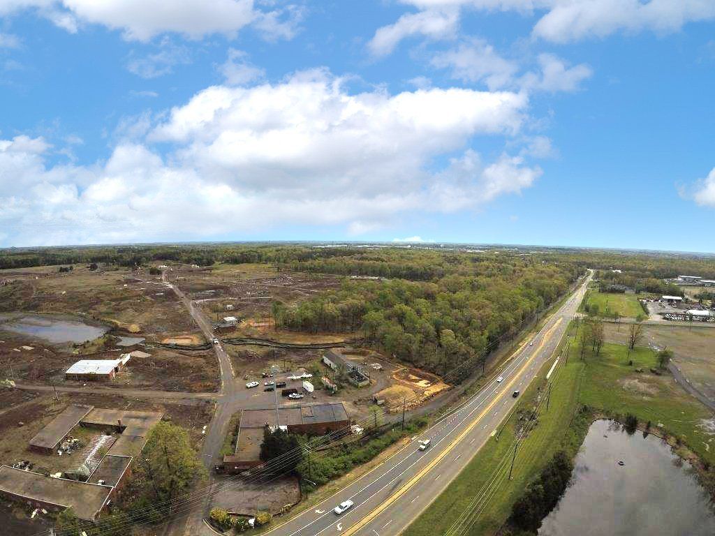 Aerial view of a highway beside a river, with open land and scattered buildings under a blue sky.