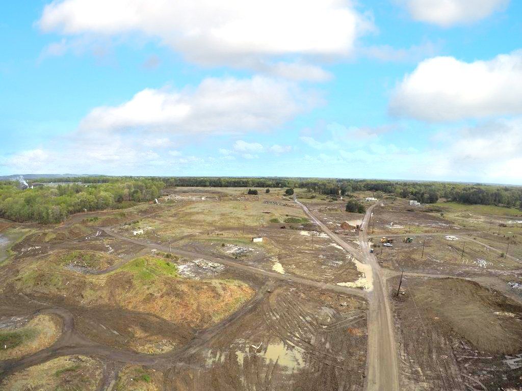Wide aerial view of a barren, cleared landscape with dirt roads and scattered debris under a cloudy sky