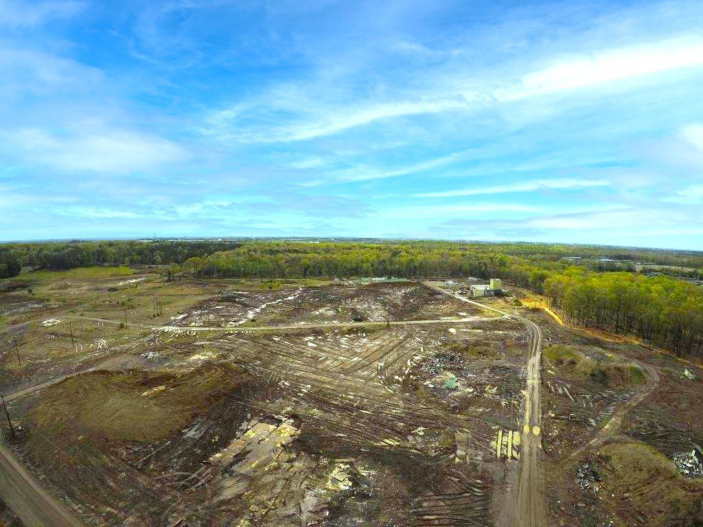 Wide barren excavation site with muddy ground and green forest under a blue sky