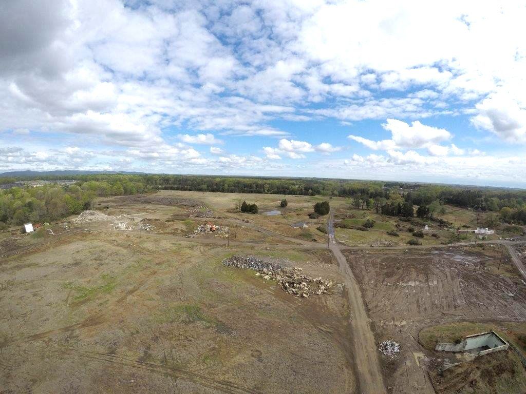 Wide landscape of a cleared dirt field with a road, scattered trees, and a cloudy sky