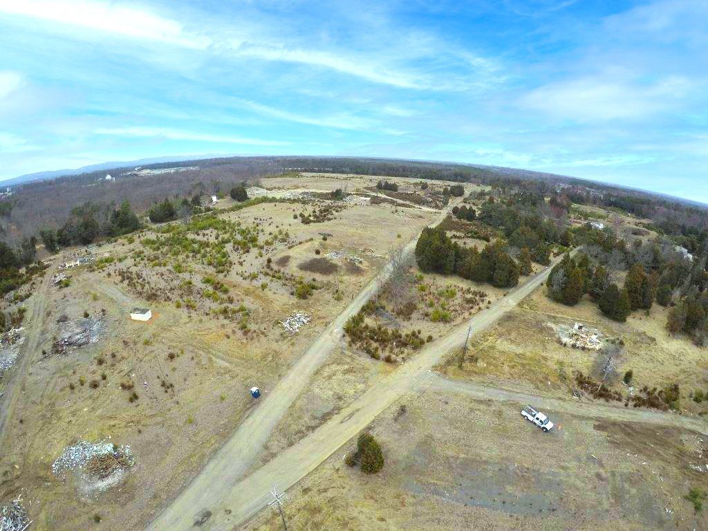 Aerial view of a dirt road crossing a barren landscape with sparse trees and scattered rocks under a blue sky