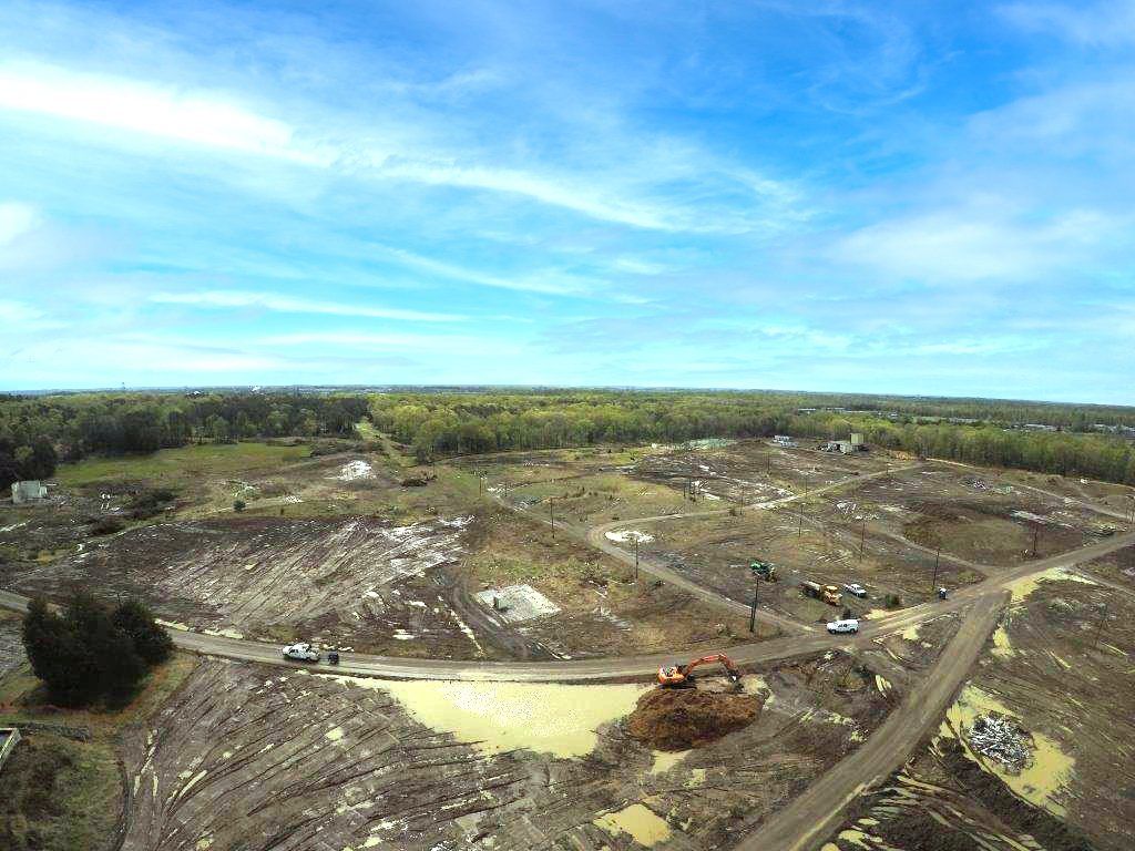 Aerial view of a cleared construction site with dirt roads, machinery, and a blue sky overhead