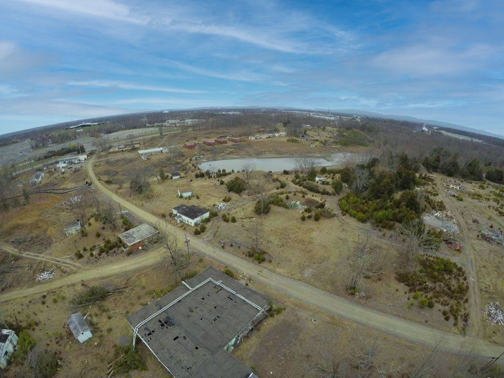 Aerial view of a rural landscape with dirt roads, scattered houses, and a small pond under a blue sky