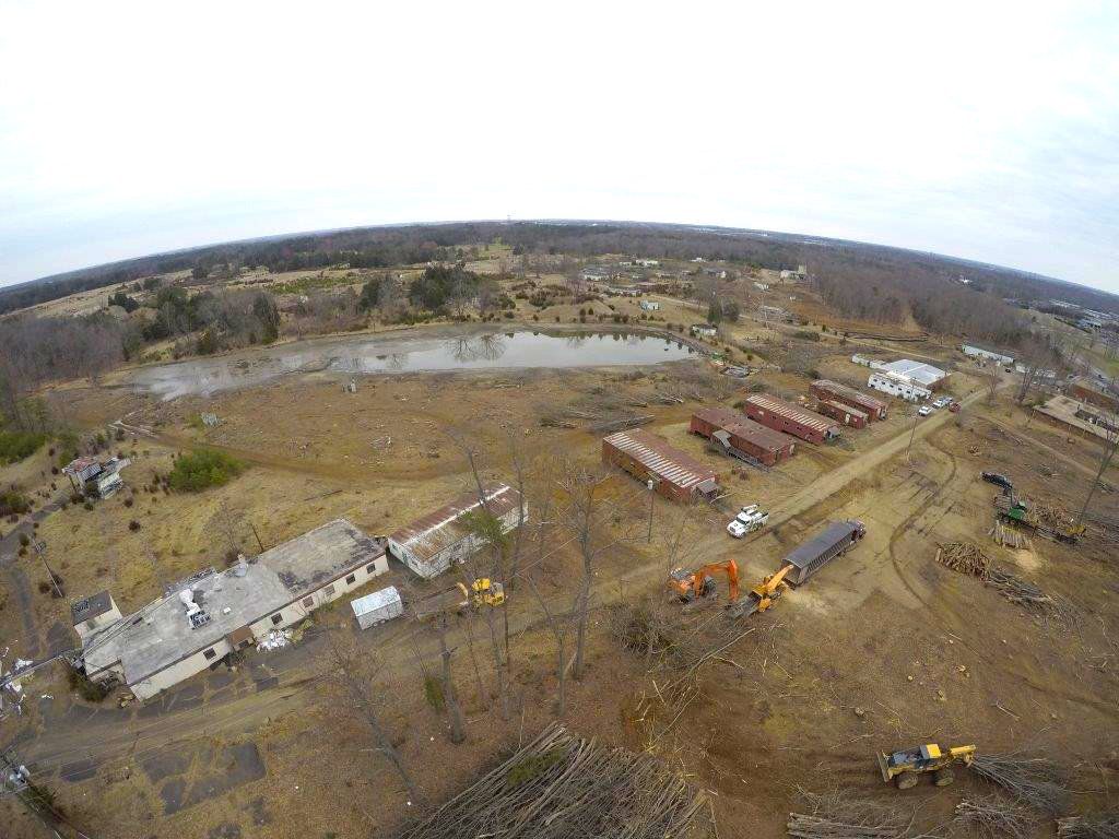 Aerial view of a construction site with dirt roads, heavy equipment, and scattered buildings near a pond