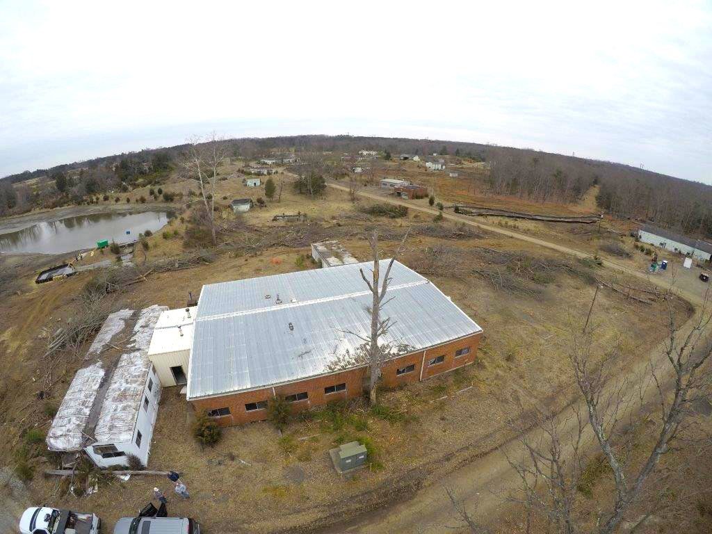 Aerial view of a rural farm with a large metal-roofed barn, trailers, and bare trees.