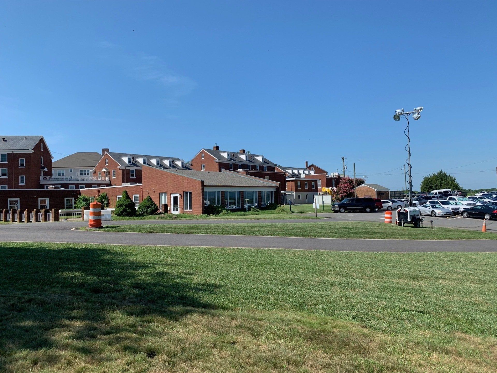 Brick buildings beside a grassy field and parking lot under a clear blue sky