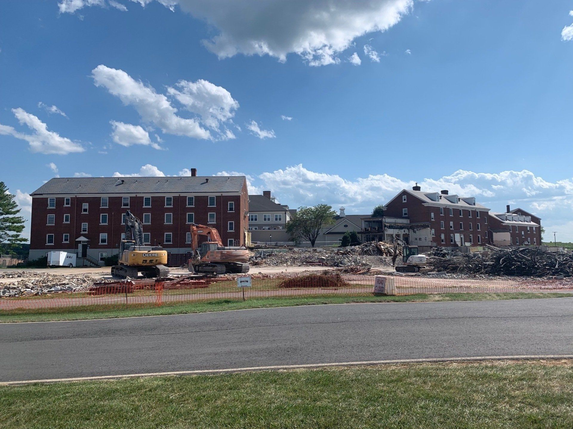 Brick buildings under construction beside a road on a sunny day with scattered clouds