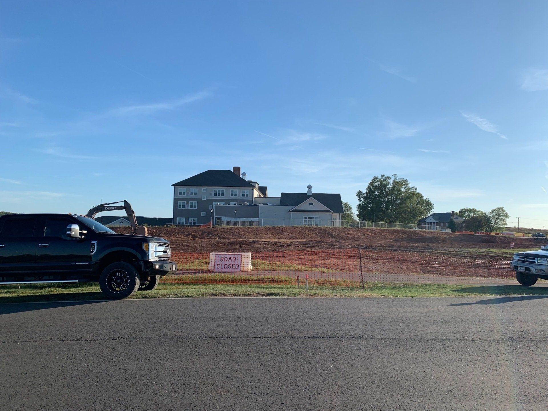Black pickup trucks on a roadside with a house and construction fencing in the background