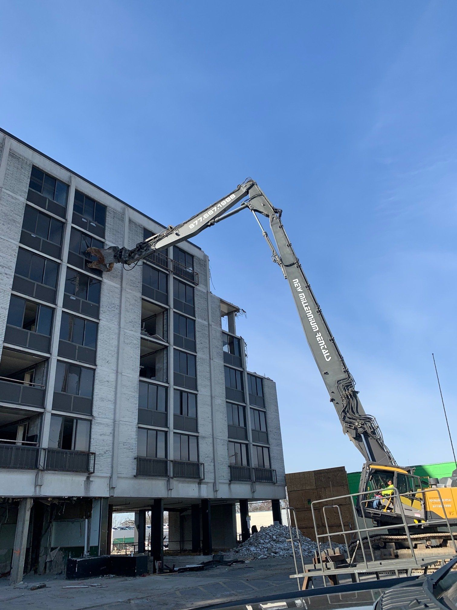 Construction lift reaching toward a gray apartment building under a blue sky