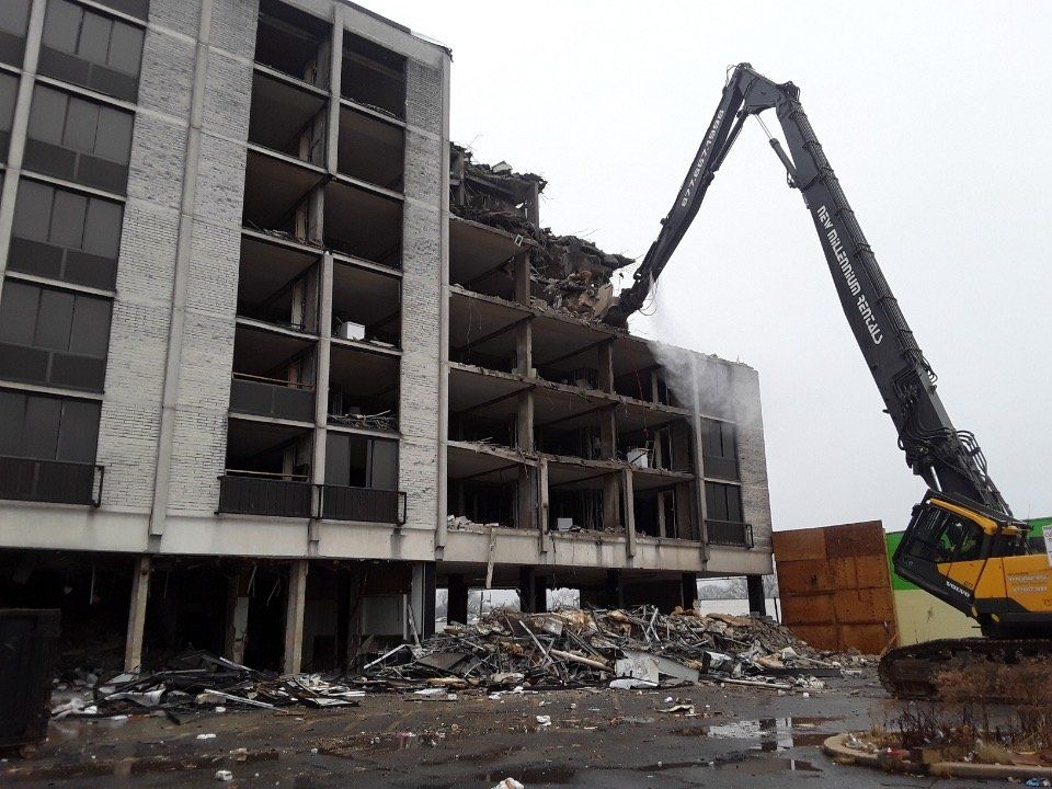 Construction excavator demolishing a partially collapsed multi-story building with rubble in front