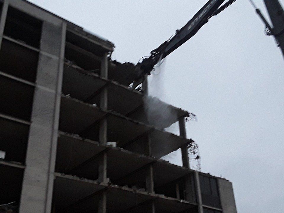 Crane demolishing the top of a concrete building against a gray sky