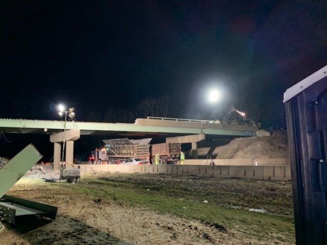 Collapsed bridge at night with debris under bright work lights and a partially intact span.