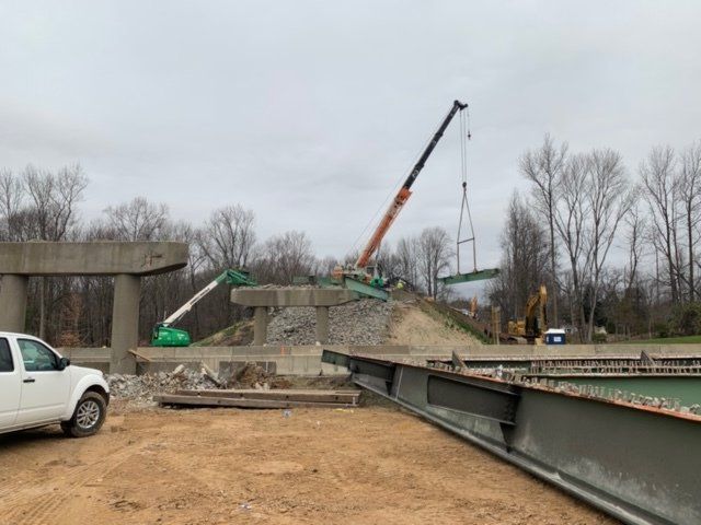 Construction site with crane lifting a concrete slab beside a bridge under repair