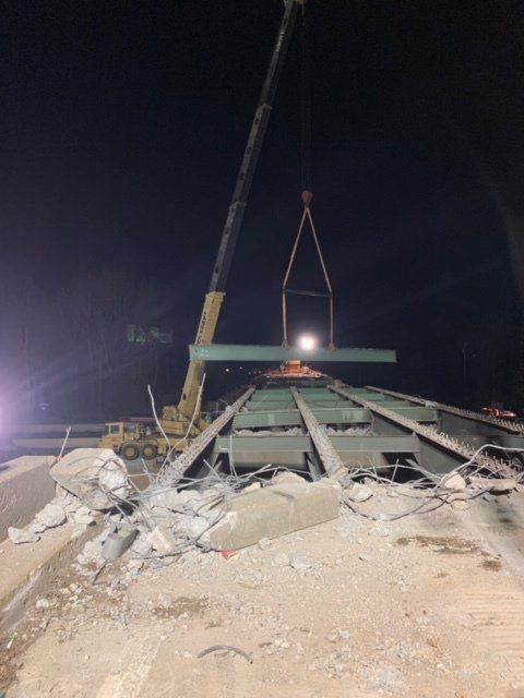 Nighttime demolition site with a crane lifting concrete debris from a collapsed roof.