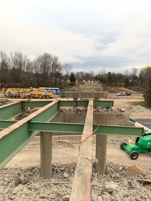 Construction site with green steel beams, concrete supports, and heavy equipment on a gravel foundation