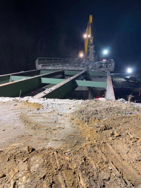 Nighttime construction site with a drilling rig and green steel beams on muddy ground.