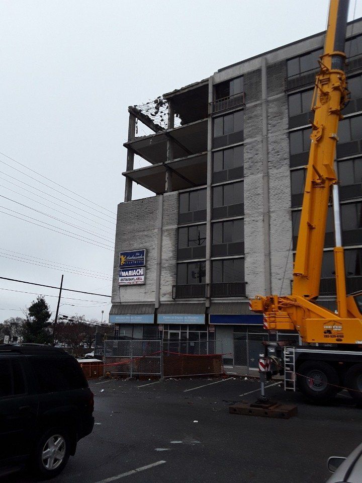 Partially demolished building with a large yellow crane on a wet street during construction or repair