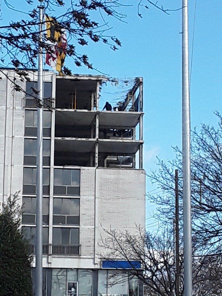 Partially demolished multi-story building with exposed concrete floors and a crane against a blue sky