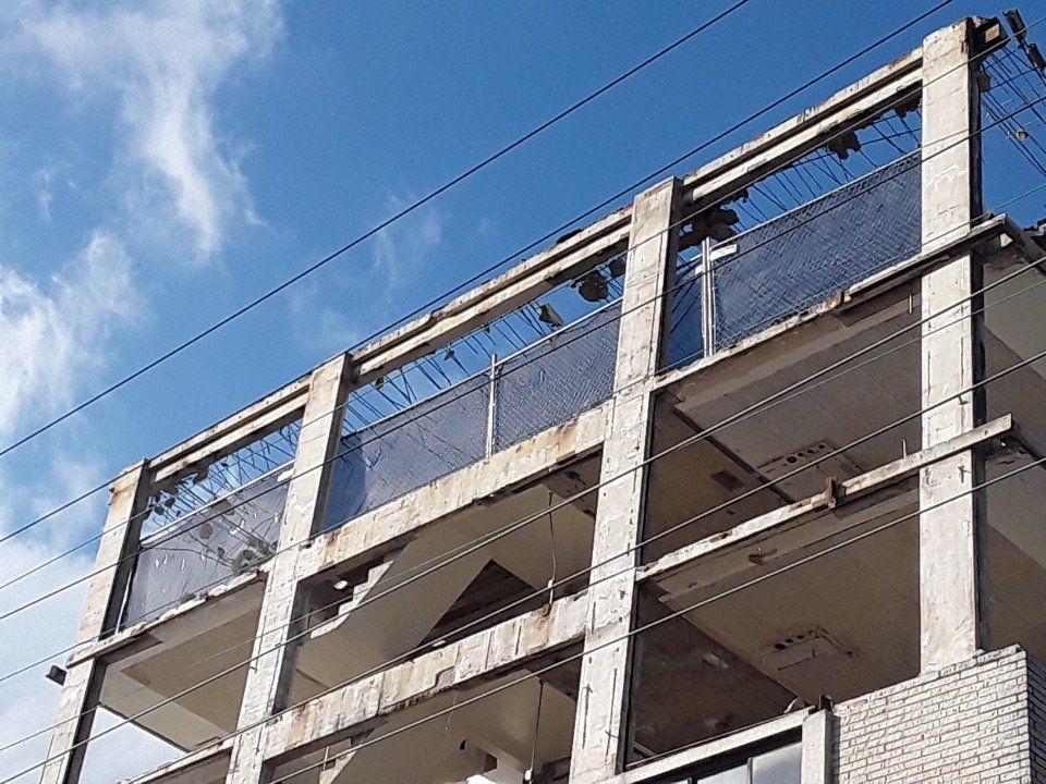 Partially built concrete building against a blue sky, with exposed beams and safety netting.