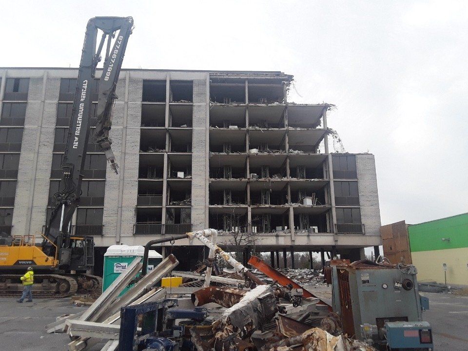 Demolished parking garage with excavator and rubble in front of a partially collapsed concrete building