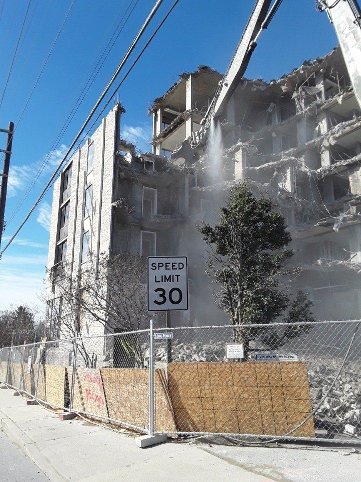 Demolished building with dust and scaffolding beside a sidewalk, with a 30 mph speed limit sign in front
