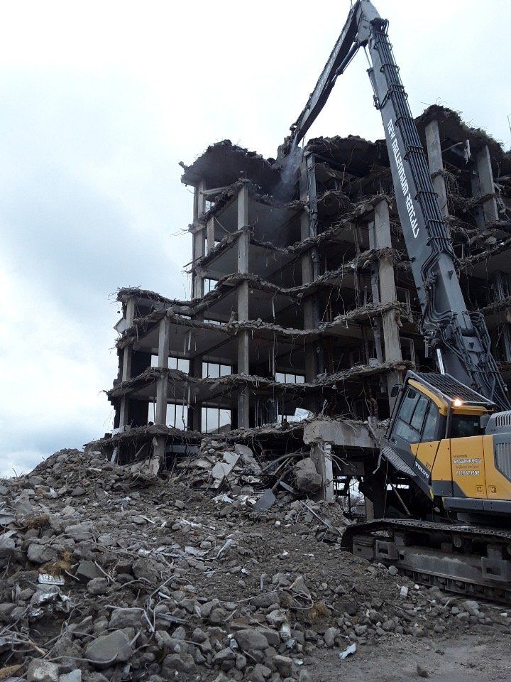 Demolished concrete building with rubble in foreground and excavator arm tearing down upper floors